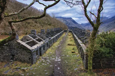 View of the abandoned stone barracks at Dinorwic slate quarry in a valley, with bare trees and mountains under a cloudy sky.