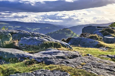 View of Dinas Bran Castle and surrounding hills from a rocky ridge under a cloudy sky.