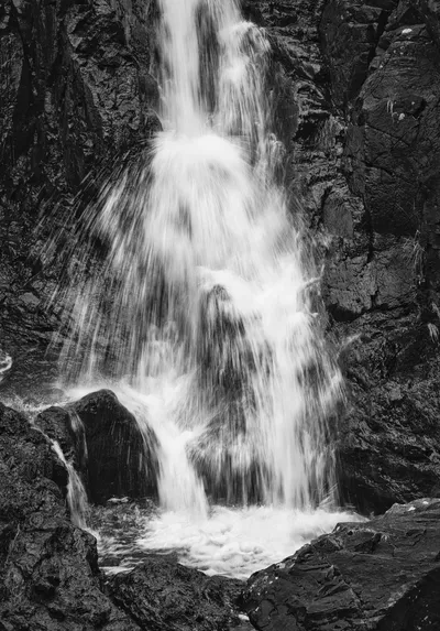Black and white long exposure photograph of a waterfall cascading over dark, textured rocks, with blurred white water.