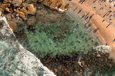 Aerial view of Bronte Beach with people sunbathing on the sand and swimming in the clear turquoise rock pool and ocean.
