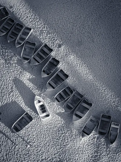 Overhead view of many small boats pulled up onto a sandy beach, with strong shadows.